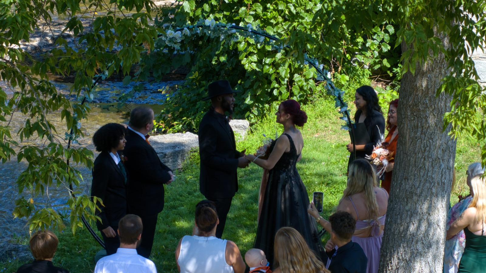 Outdoor wedding ceremony beside the creek, under a floral arch.