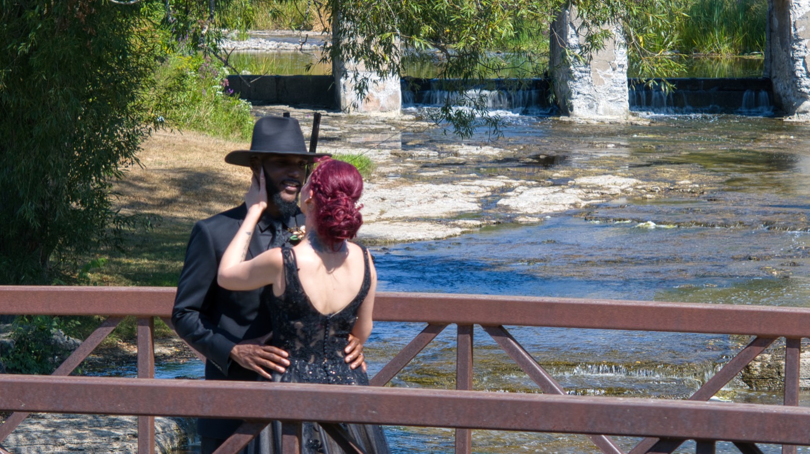 The couple standing on the footbridge with the creek and small falls behind them.