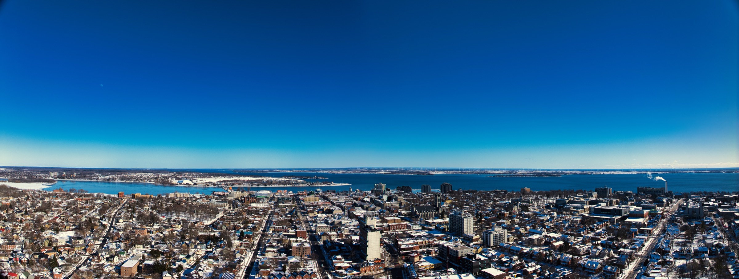 Wide aerial of downtown Kingston in snow, with the lake and river on the horizon.