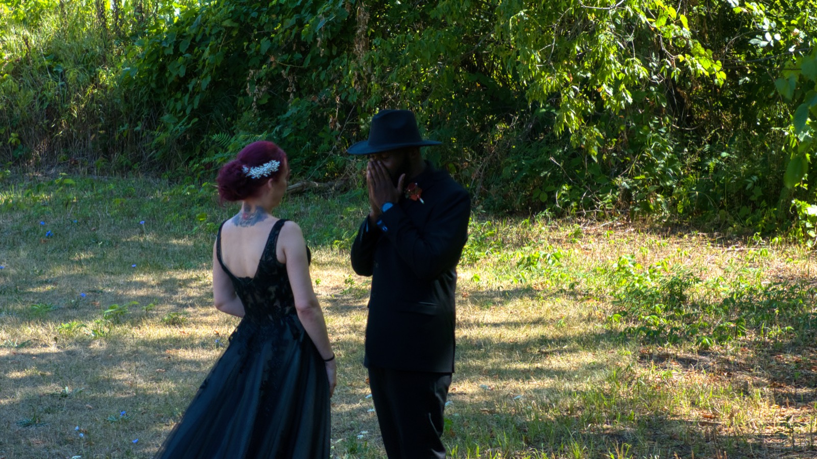 A bride and groom during a first look on the grass, trees behind them.