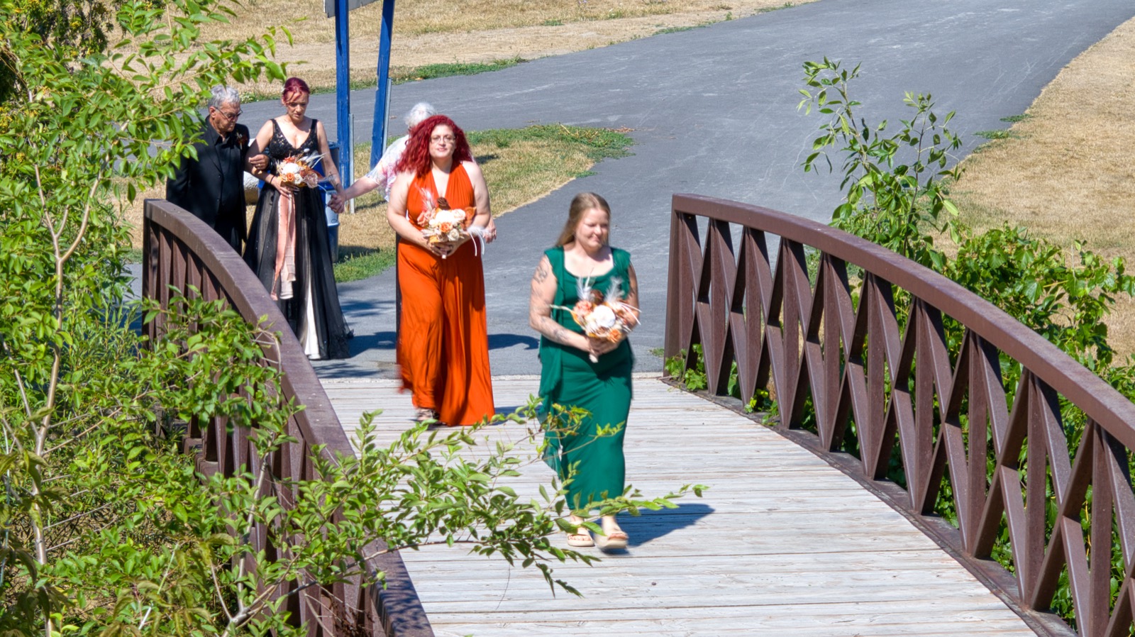 Wedding party walking across the wooden footbridge with bouquets.
