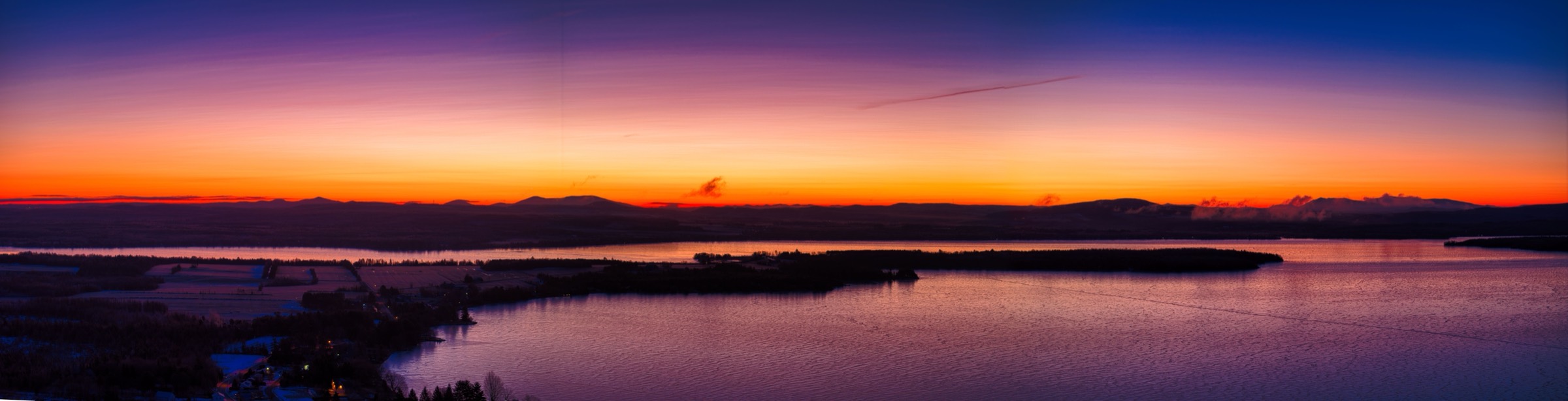 Panorama of a lake at sunrise, orange sky over a dark shoreline.