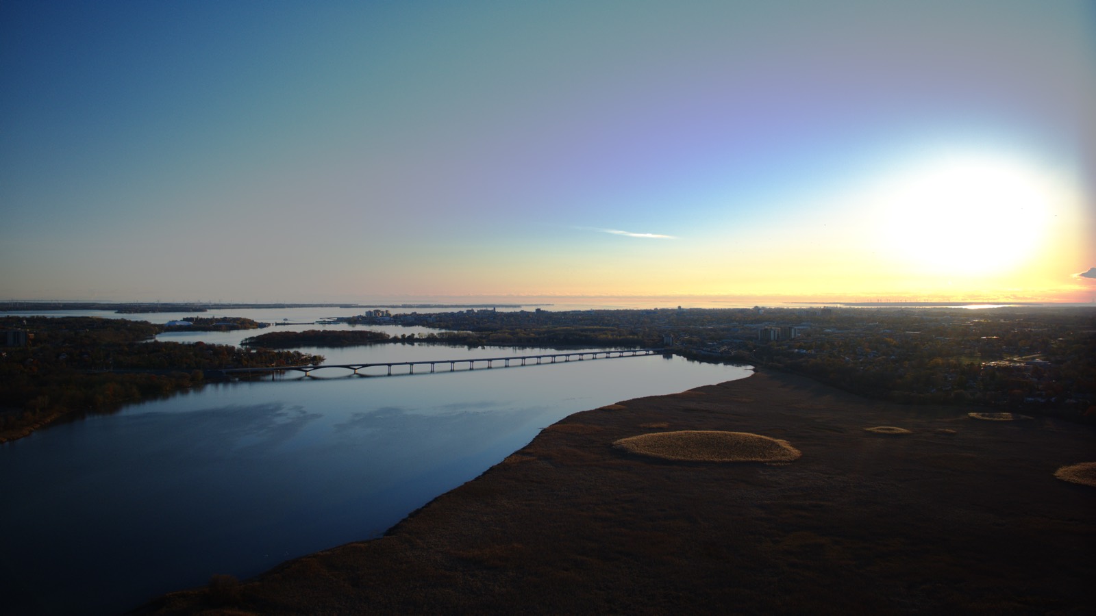Aerial view of a bridge over the river at sunset, with the sun low on the right.